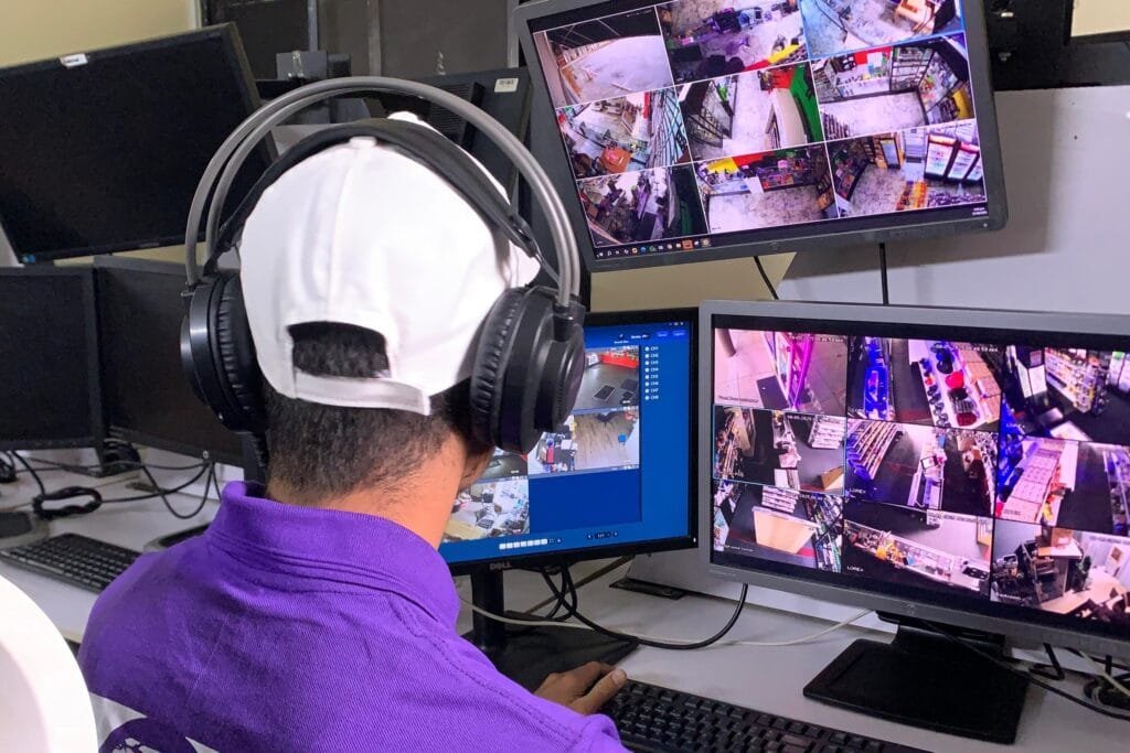 Security operator monitoring live CCTV feeds of a gym or retail space from a control room.