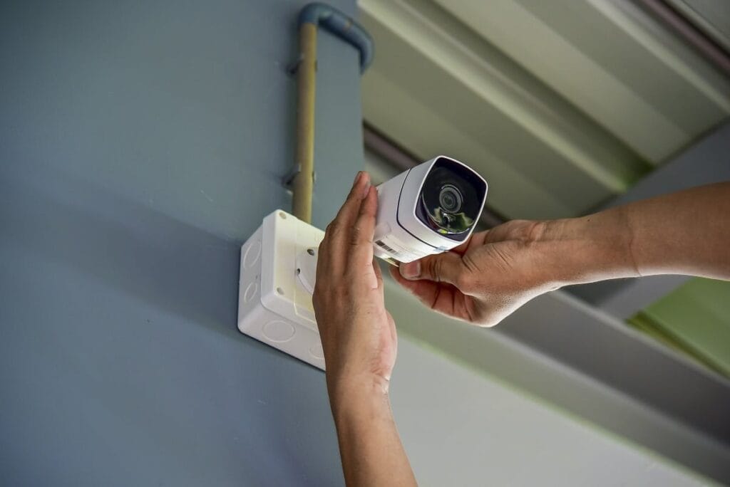 Hands installing a white security camera on a wall, preparing for professional CCTV monitoring services.