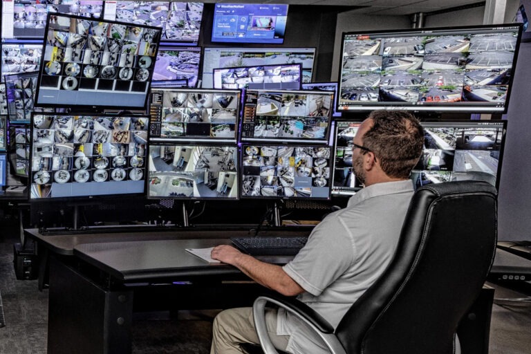 Security technician monitoring numerous CCTV screens in a control room, showcasing Live CCTV Monitoring and Remote CCTV Monitoring Services. 