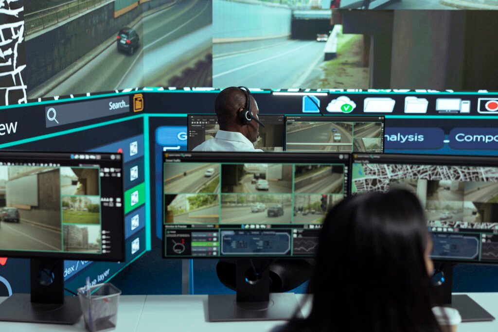 Security professionals at a command center performing Live Video Monitoring on multiple screens displaying real-time traffic and road surveillance, illustrating dedicated Screen Monitoring Services.