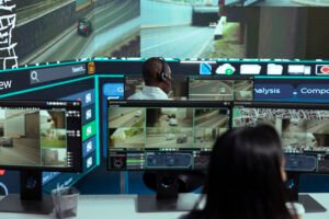 Security professionals at a command center performing Live Video Monitoring on multiple screens displaying real-time traffic and road surveillance, illustrating dedicated Screen Monitoring Services.