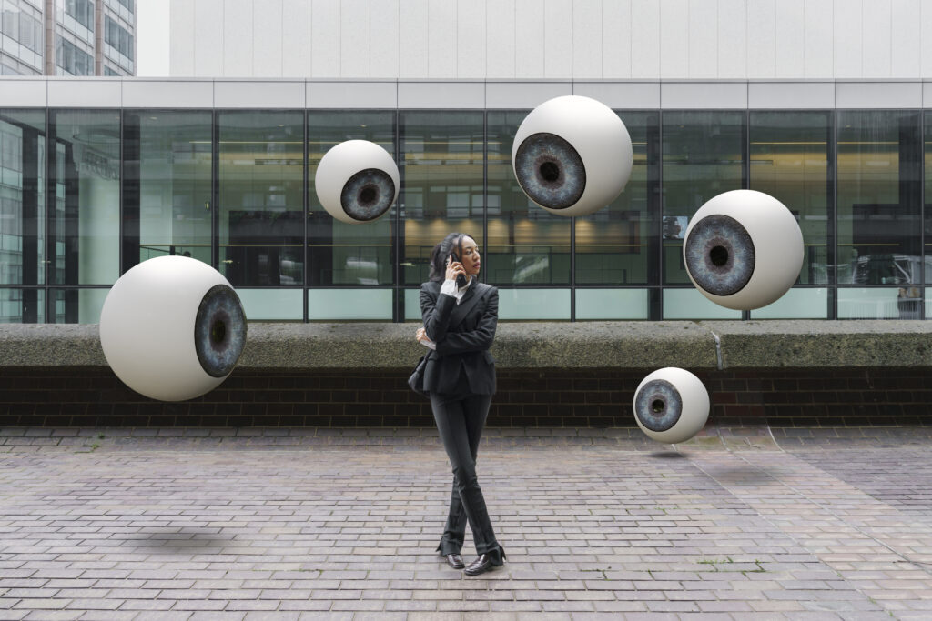 A collection of images depicting the pervasive nature of security (floating eyeballs in an urban setting) and a security operator performing live CCTV monitoring on multiple screens, representing professional CCTV monitoring services from GCCTVMS.