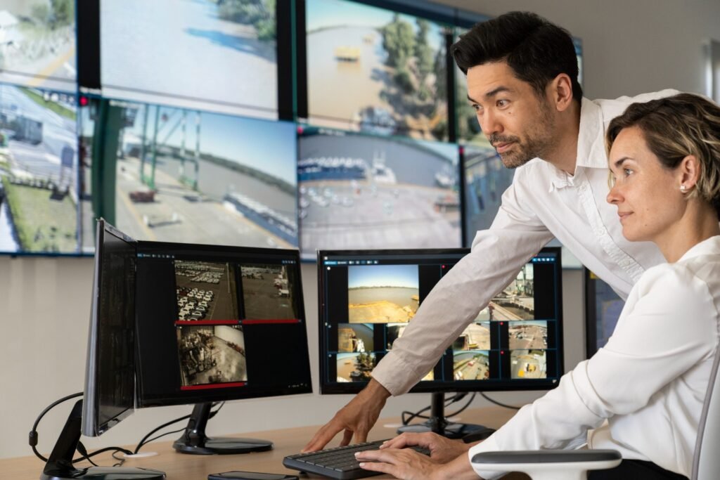 Two professionals analyzing multiple camera feeds on large monitors in a control room, symbolizing advanced video monitoring services and remote surveillance.
