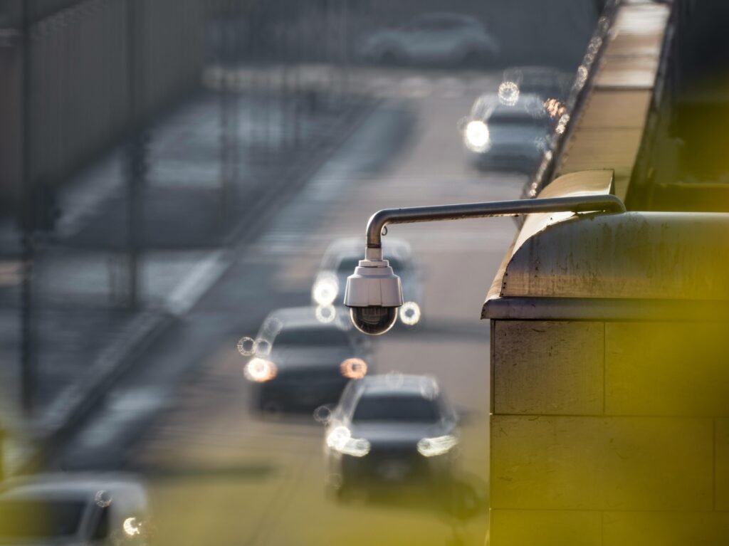 A dome-style CCTV camera mounted on a bridge or overpass railing, overlooking blurred vehicle traffic, illustrating the function of a CCTV monitoring company in public CCTV surveillance.