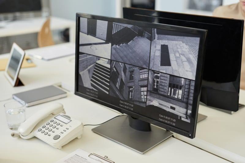 Close-up of a desk with a landline phone and a monitor showing six external CCTV monitoring views.
