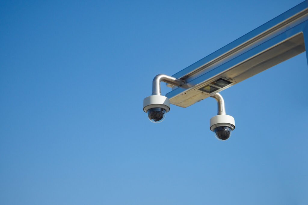 Two professional white dome cameras mounted on a sleek metal arm against a clear blue sky, demonstrating high-quality video surveillance infrastructure