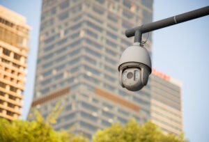 A white PTZ dome camera mounted on a metal arm overlooking an urban landscape, illustrating the role of surveillance and CCTV surveillance in city safety