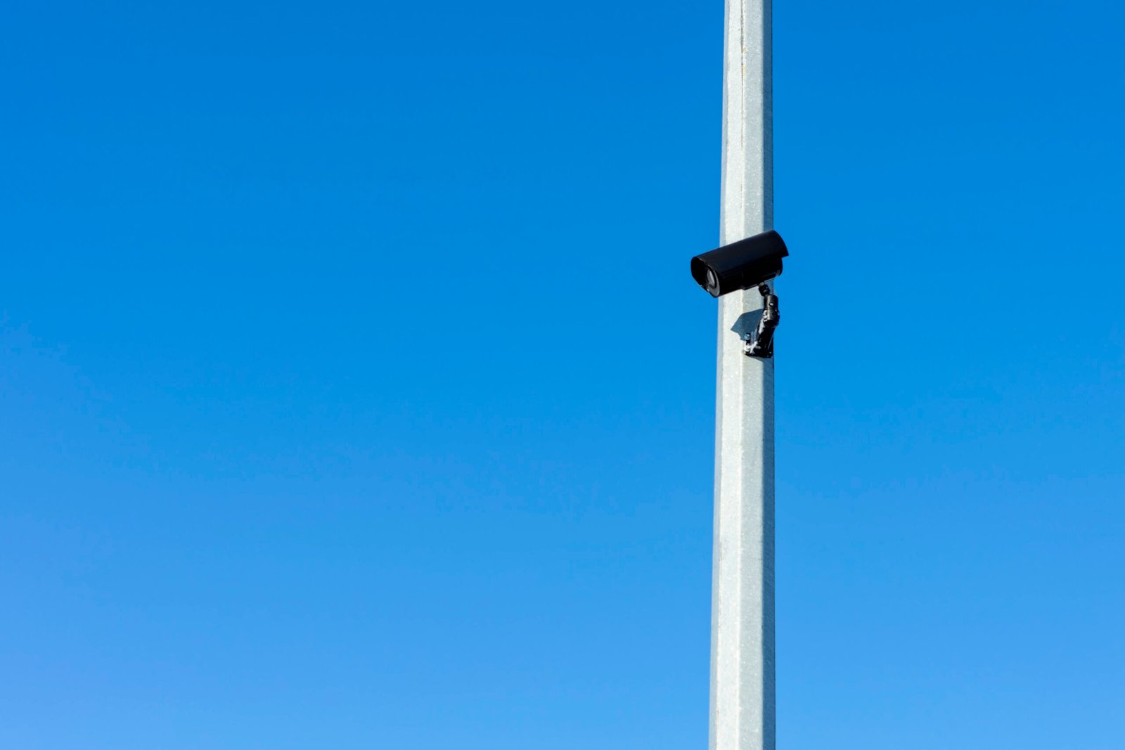 A black security camera mounted high on a metal pole against a clear blue sky, illustrating the infrastructure needed for effective CCTV surveillance and crime prevention