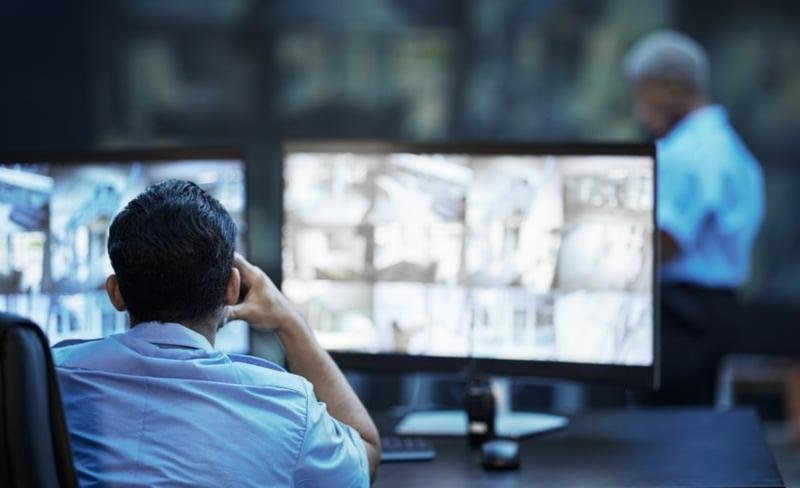 A security operator in a blue shirt watching multiple screens, providing affordable CCTV monitoring and surveillance services