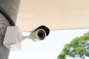 A close-up of a white bullet-style security camera with infrared sensors mounted on a concrete pillar, representing a professional Camera Monitoring Service installation for Business Security and Home Security Monitoring