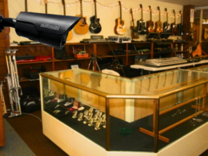Alt Text: A prominent black bullet security camera actively overlooking a retail space filled with guitars and a glass display case of jewelry, illustrating the critical need for CCTV monitoring for pawn shops to ensure robust pawn shop security through reliable remote CCTV monitoring services.