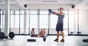 A man actively exercises with a kettlebell on a spacious gym floor while two prominently mounted ceiling dome cameras provide dedicated CCTV Monitoring for Gyms, ensuring member safety through a reliable security service and continuous video surveillance.