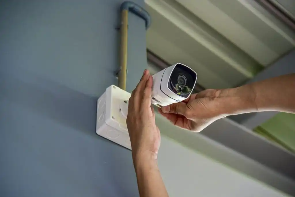 Hands installing a white security camera on a wall, preparing for professional CCTV monitoring services.