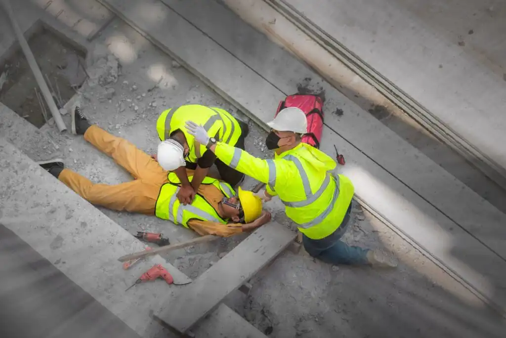 Workers attending to an injured colleague on a construction site, demonstrating the need for effective workplace incident reporting and safety protocols.