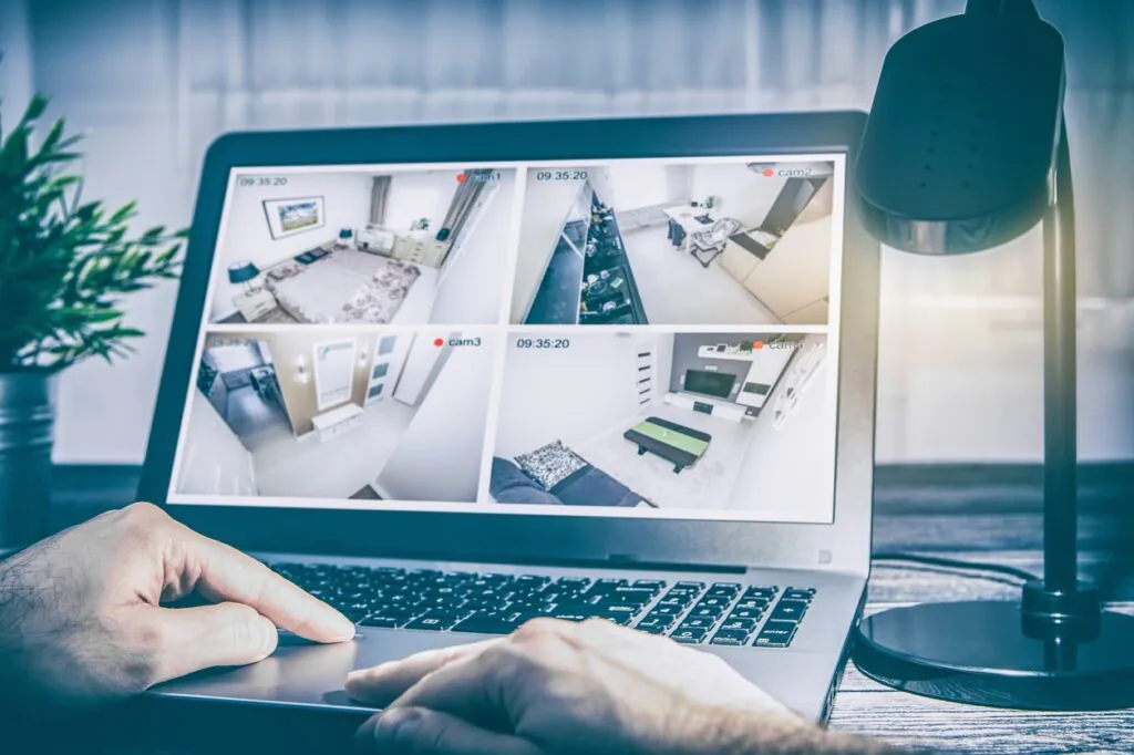Laptop screen showing four live CCTV camera feeds of a home interior, representing remote monitoring and 24/7 CCTV monitoring services.