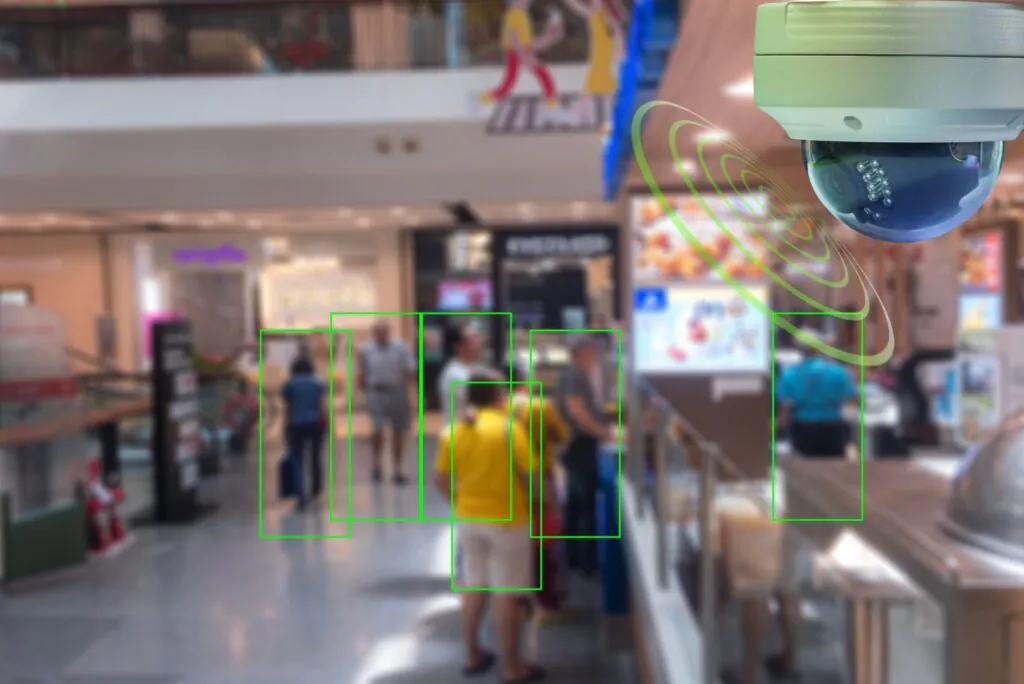 Security camera with green detection zones highlighting people in a busy mall, representing Remote CCTV Monitoring Services and Live CCTV Monitoring.
