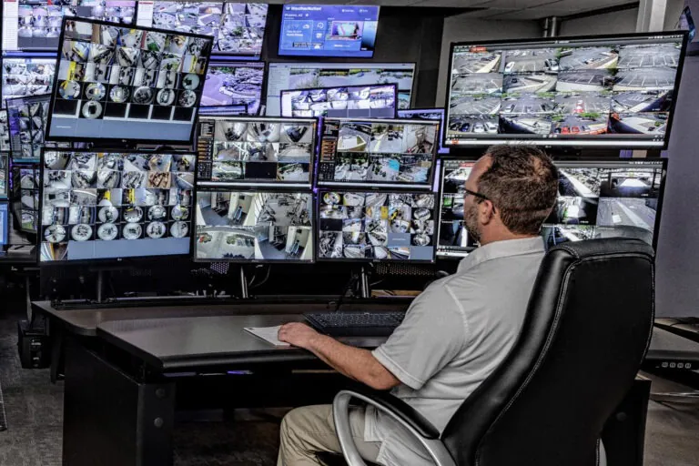 Security technician monitoring numerous CCTV screens in a control room, showcasing Live CCTV Monitoring and Remote CCTV Monitoring Services.