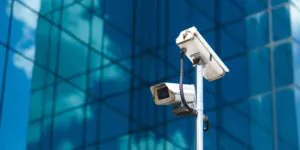 Outdoor security cameras mounted on a pole in front of a modern glass building, representing CCTV Monitoring in UK and Business Security solutions.