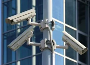A montage of images illustrating end-to-end security, including outdoor and indoor surveillance cameras, remote control room operators, mobile monitoring views, and access control systems, all centered on dedicated CCTV Monitoring Services