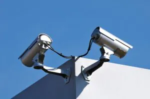 Two silver cylindrical security cameras mounted on the corner of a commercial building against a clear blue sky, illustrating professional Video Surveillance for business protection.