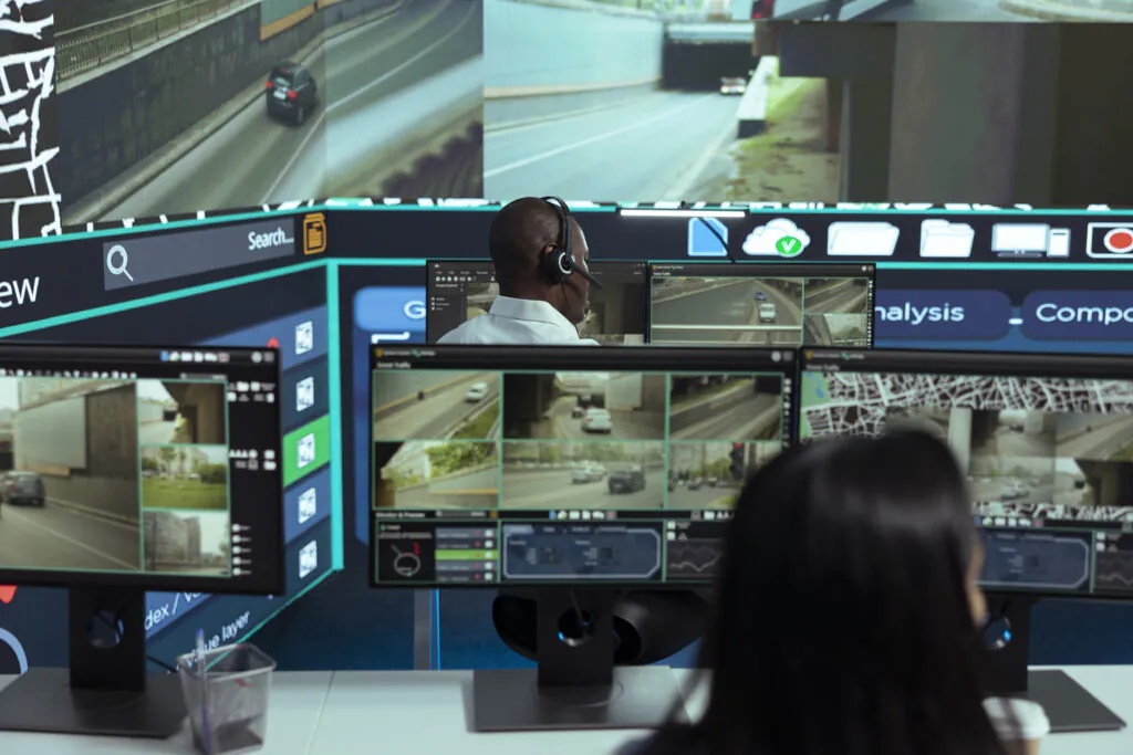 Security professionals at a command center performing Live Video Monitoring on multiple screens displaying real-time traffic and road surveillance, illustrating dedicated Screen Monitoring Services.