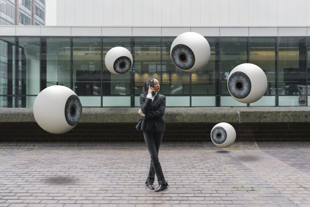 A collection of images depicting the pervasive nature of security (floating eyeballs in an urban setting) and a security operator performing live CCTV monitoring on multiple screens, representing professional CCTV monitoring services from GCCTVMS.