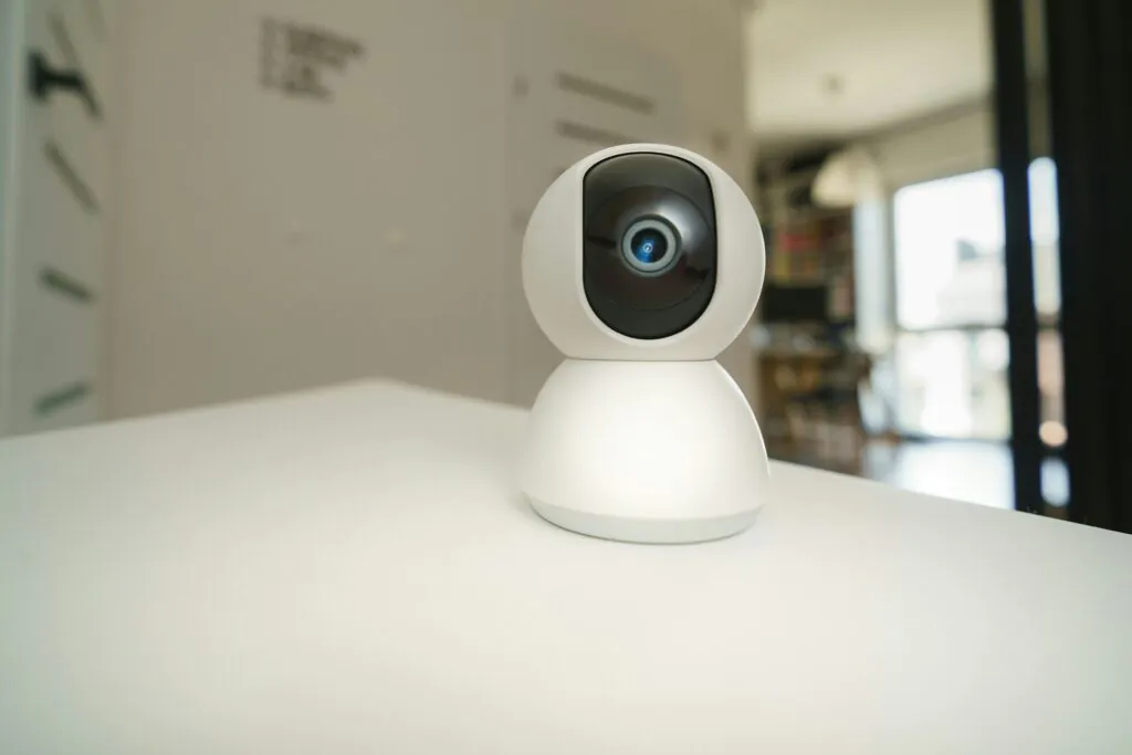 A small white indoor security camera (Nanny Cams) on a shelf in a child's room with stuffed animals, symbolizing discreet Nanny Cams Monitoring for family safety.
