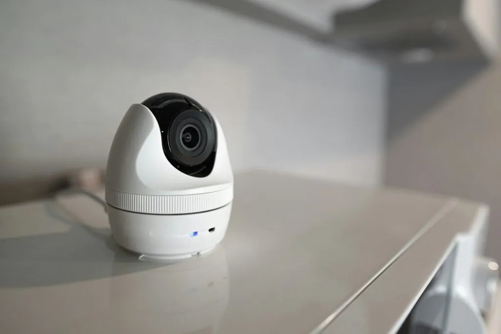A small white, modern dome camera on a white surface indoors, illustrating a contemporary solution for discreet Nanny Cams Monitoring and indoor Home Surveillance.