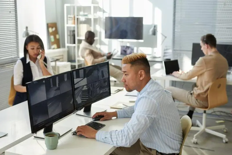 Diverse office setting with staff providing CCTV monitoring on dual screens.