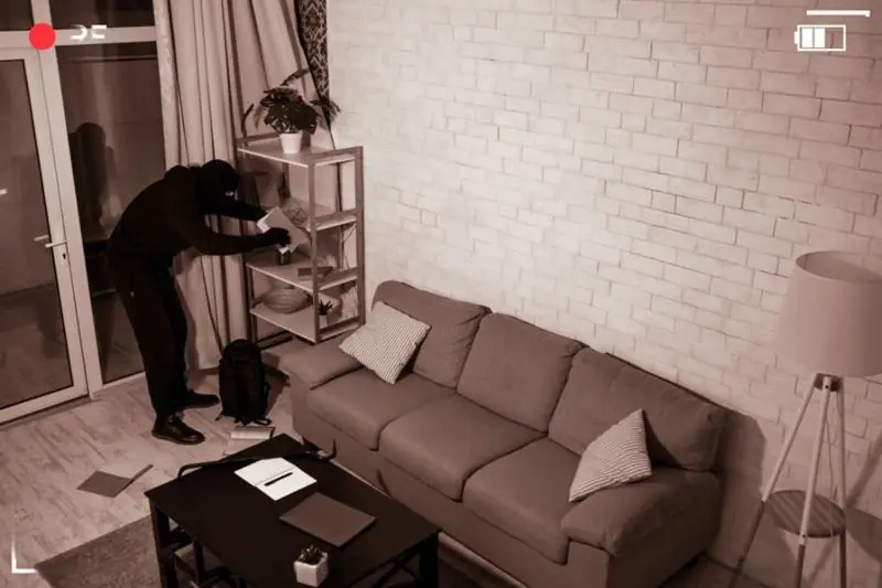 Night vision view of a burglar wearing a mask rummaging through a shelf, captured by CCTV Surveillance.