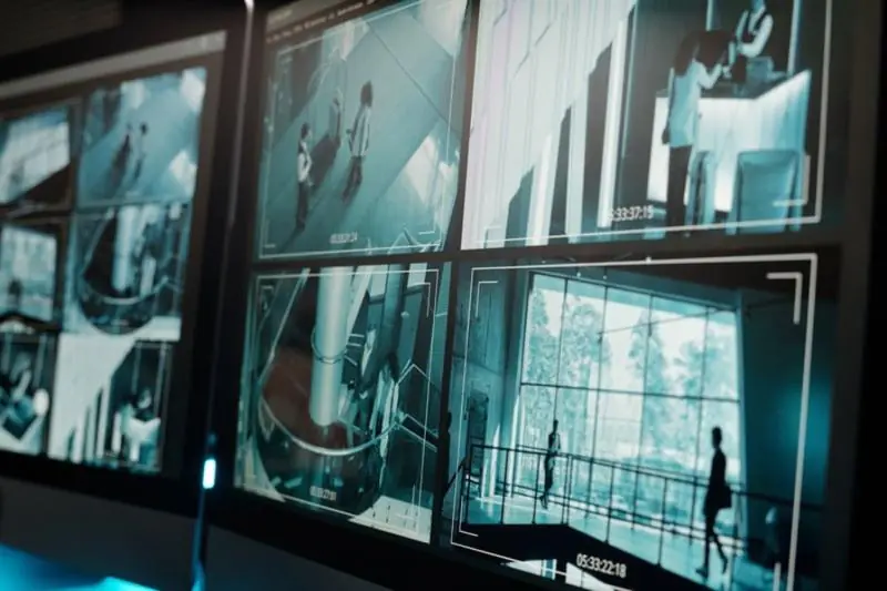 Multiple computer monitors displaying a grid of blue-toned surveillance feeds from a modern commercial interior with people moving, demonstrating the scope of a CCTV Monitoring Provider's service.