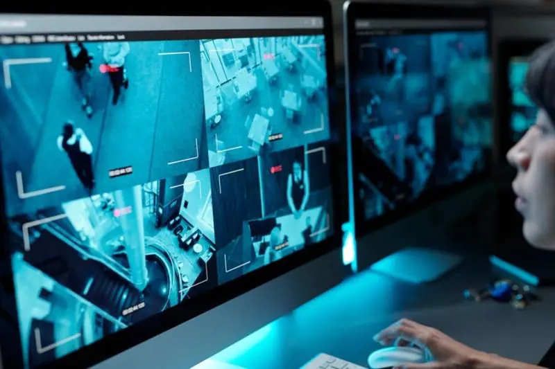Female security operator watches live feeds on multiple monitors with blue light, confirming Professional Security Monitoring.