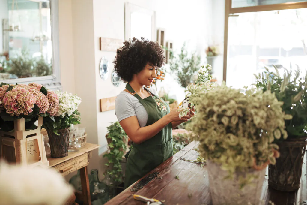 Woman with curly hair arranging flowers in a bright floral shop. Enhance retail security with two-way audio.
