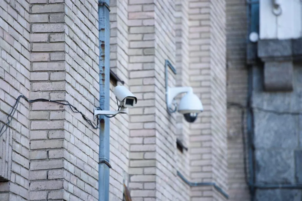 Two white security cameras, a bullet and a dome style, mounted on a brick wall for outdoor Video Surveillance