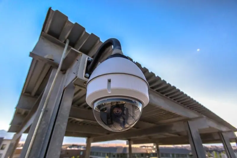 A white dome camera mounted on an outdoor metal structure, representing modern CCTV surveillance technology used for remote CCTV surveillance