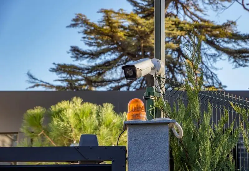 A security operator analyzes blue-tinted video feeds with detection boxes on a monitor, conducting remote CCTV monitoring to confirm human-verified alerts.