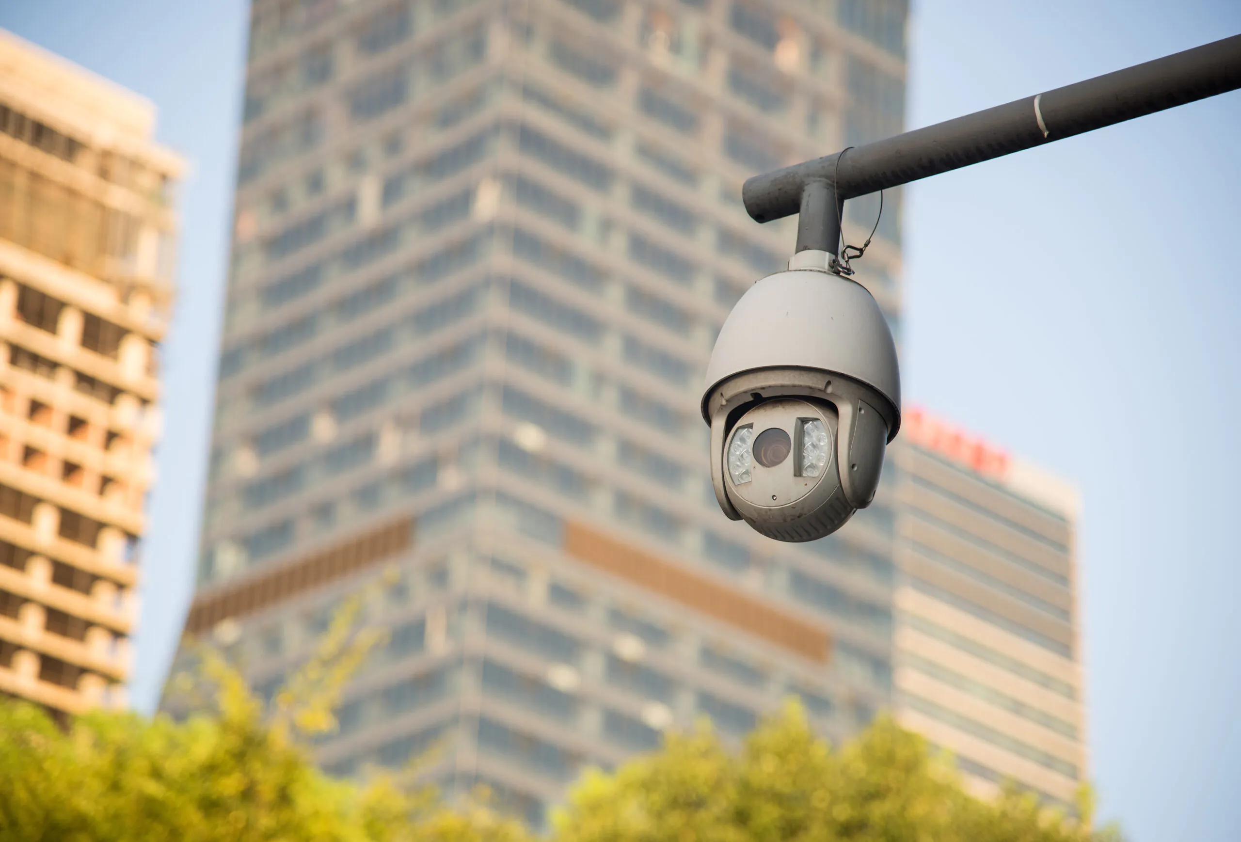 A white PTZ dome camera mounted on a metal arm overlooking an urban landscape, illustrating the role of surveillance and CCTV surveillance in city safety
