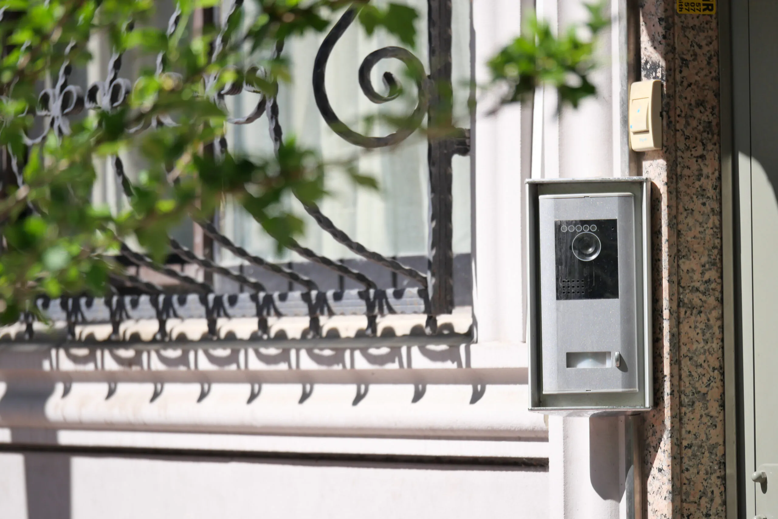 A silver video intercom doorbell mounted on a stone entrance wall, enabling remote CCTV monitoring for residential security.