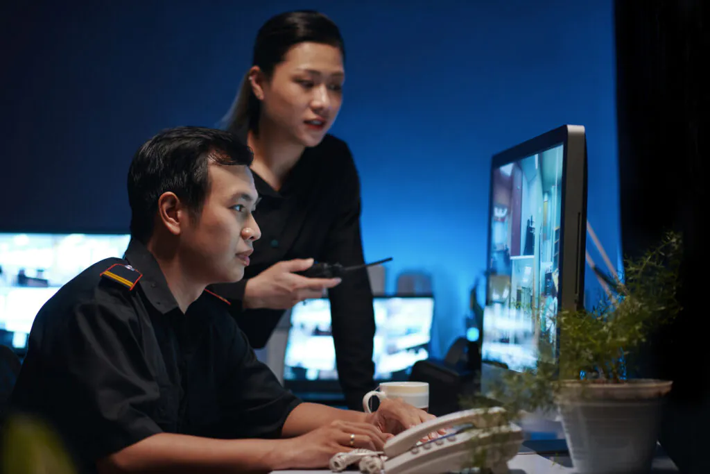 A security operator and supervisor utilizing remote CCTV monitoring services to watch live video feeds on a computer monitor.
