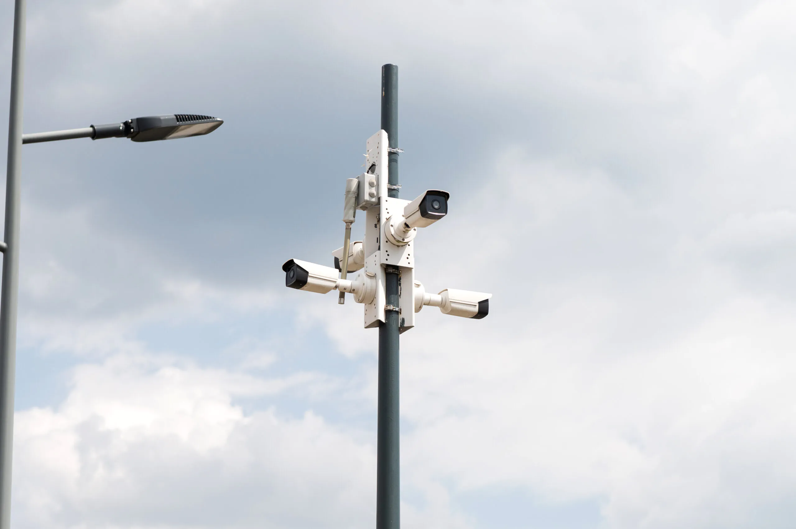 A cluster of white security cameras and a wireless transmitter mounted on a pole against a cloudy sky, illustrating a hardware setup for remote CCTV