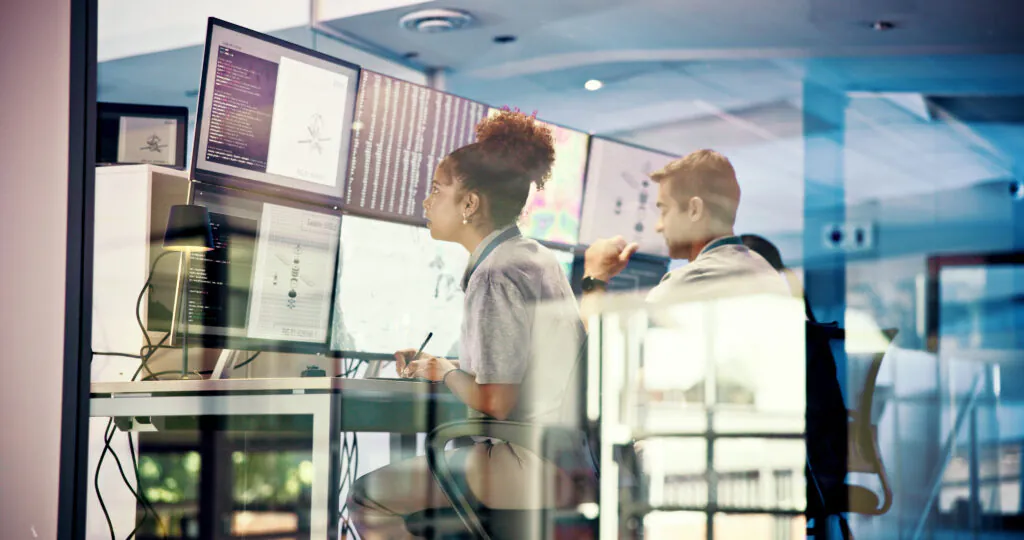 Security professionals working in a modern glass-walled office, managing remote CCTV surveillance and analyzing data on multiple monitors.