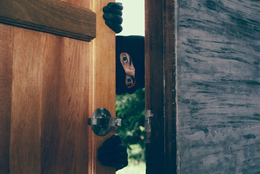 A masked intruder peeking through a cracked door, highlighting the critical need for surveillance and proactive CCTV surveillance to prevent crime