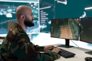 A security specialist in camouflage monitoring multiple screens, representing the high standards of Remote Doorman and remote doorman services offered by a concierge company