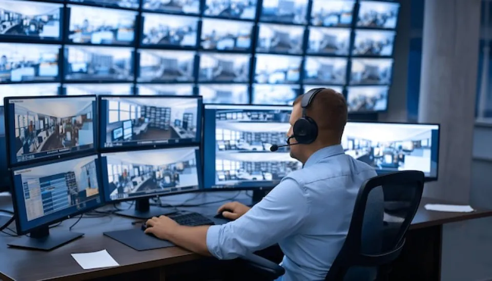 A security operator in a headset monitors multiple screens to provide virtual doorman and virtual guard services, illustrating the technology behind provider selection for property management