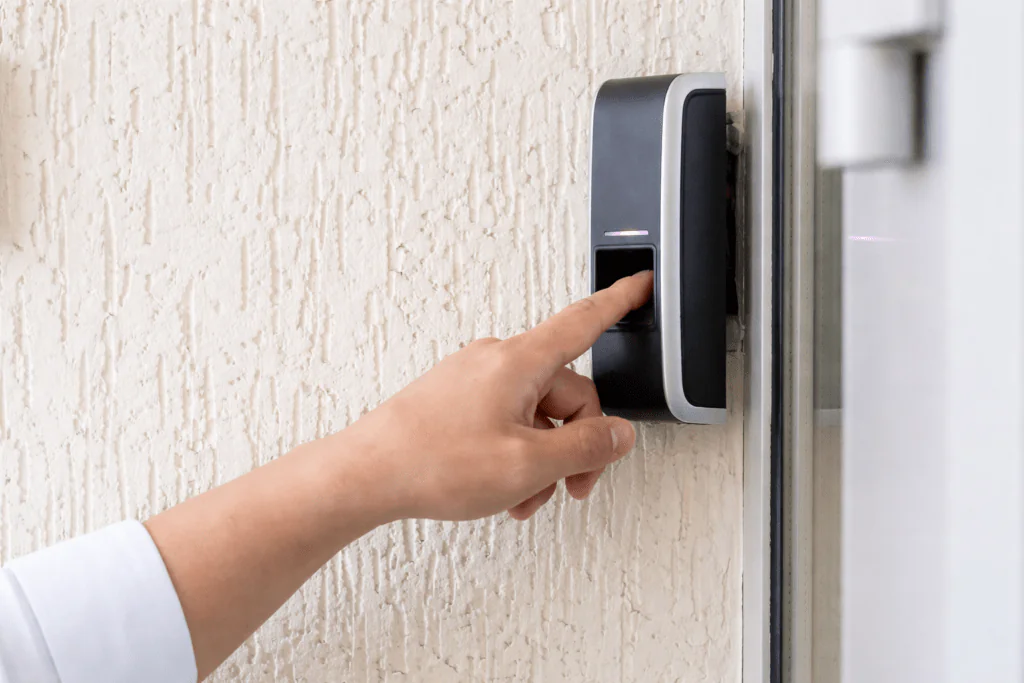 A close-up of a person's hand using a biometric fingerprint scanner on a wall-mounted unit, illustrating the secure access control features of a modern Virtual Doorman system