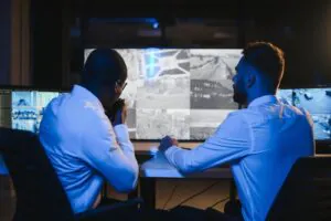 A security operator in a headset monitors multiple screens to provide virtual doorman and virtual guard services, illustrating the technology behind provider selection for property management