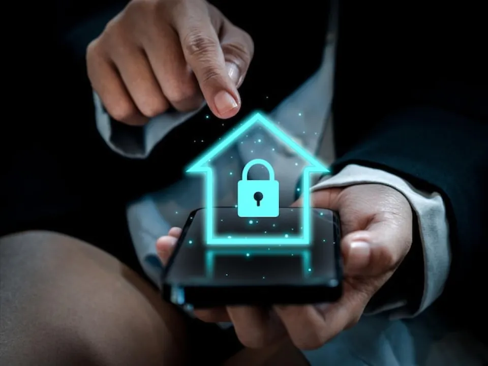 A close-up of a person holding a smartphone featuring a glowing blue digital house icon with a secure padlock, symbolizing professional CCTV Surveillance and Remote CCTV Surveillance