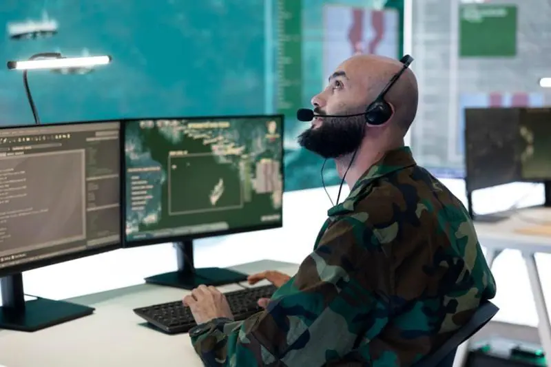 A Virtual Doorman sitting at a desk with a headset, monitoring maps and data on multiple screens to perform virtual guard services and Virtual Doorman duties.