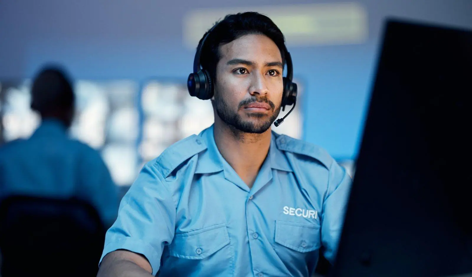A professional security operator with a headset and uniform monitoring a screen, acting as a Virtual Doorman to provide remote building security