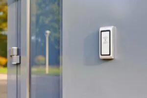 A close-up of a silver and white contactless card reader mounted on a gray door, showcasing a hardware component used in a Common Remote Doorman system for Building Security